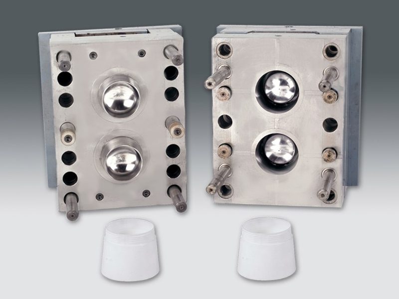 A multi-cavity injection mould open on the bench with the moulded closures still on the runner.